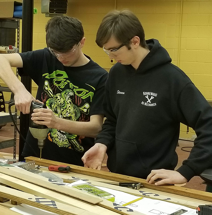 Two students drilling holes into robot part in the shop