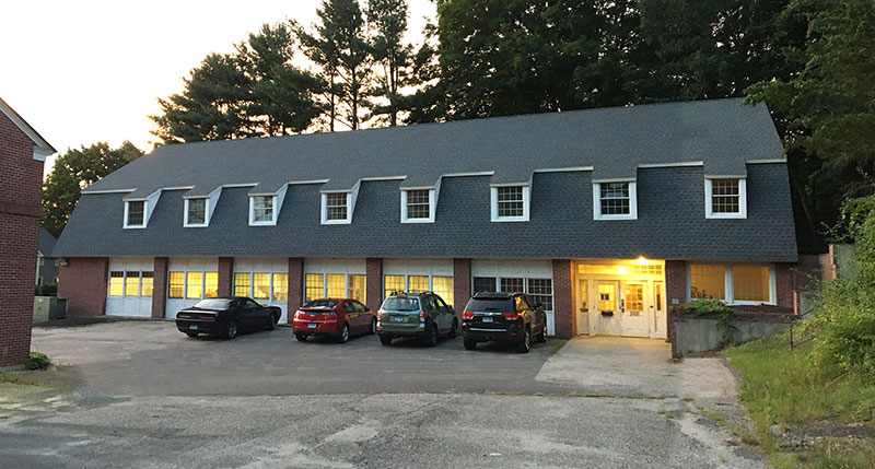 brick building at evening with lights glowing from windows, cars parked outside.