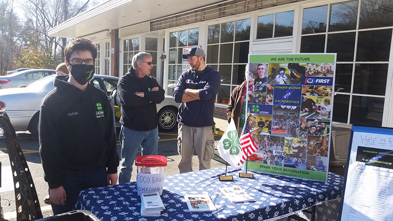 students at table in grocery store parking lot during food drive event