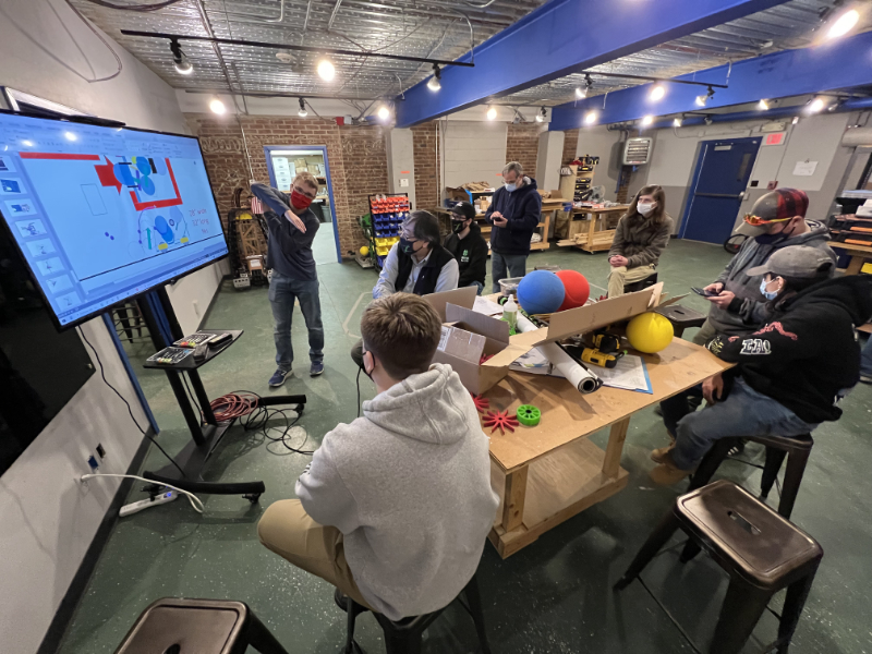 first meeting in new space: students sitting with robot parts watching presenter at smart screen