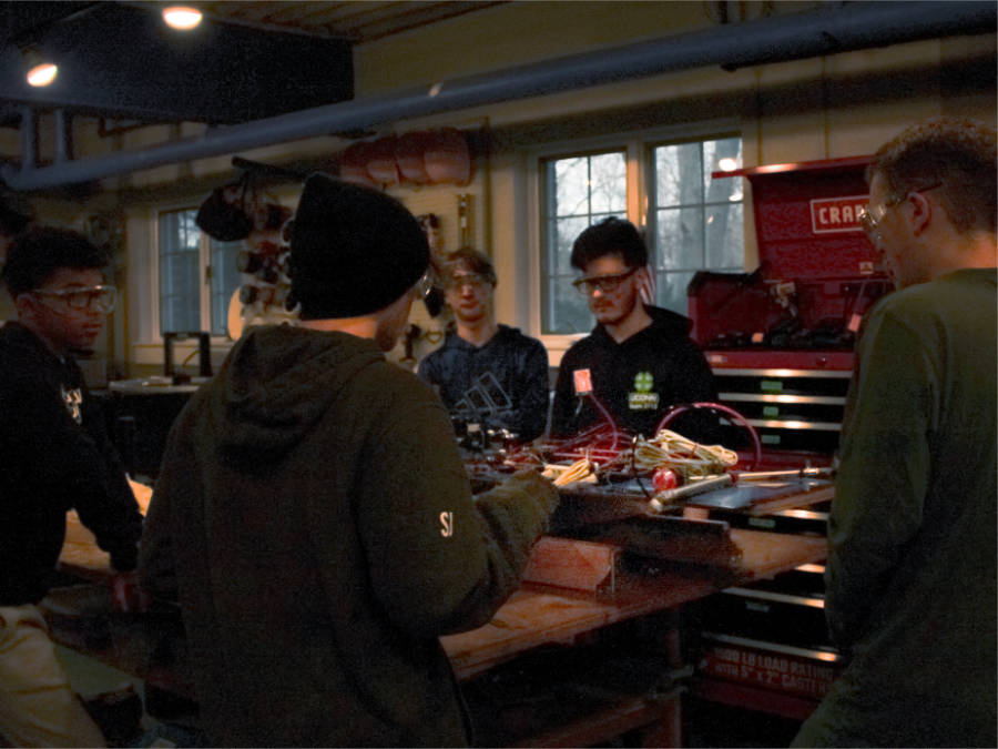 students and mentor gathered around robot on shop bench