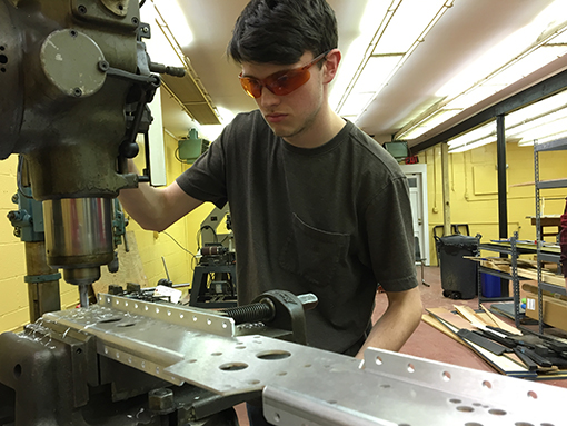 Student drilling holes into metal at the Bridgeport Milling Machine in the shop