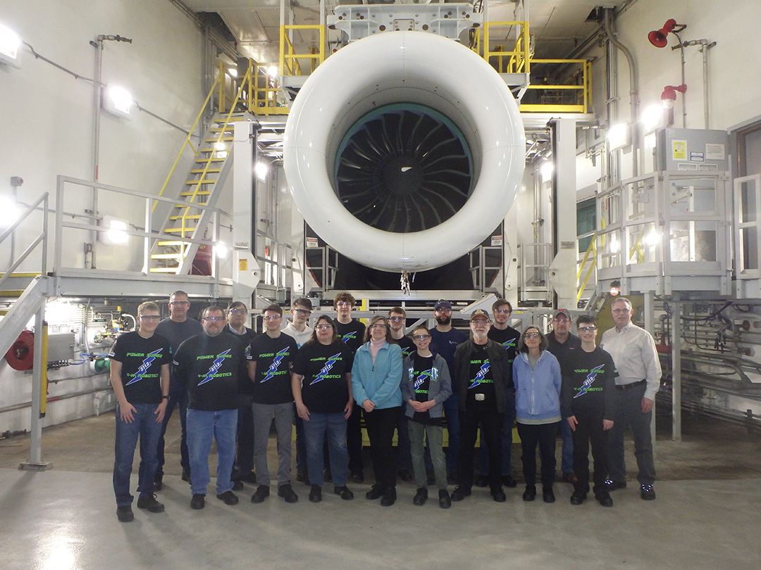 Team group portrait in front of at jet engine in the testing facility.