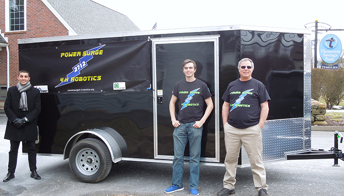Image of two members and bank manager standing in front of team trailer the bank helped purchase.