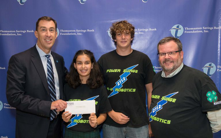 Image of bank president presenting grant check to two students and a mentor of the team.