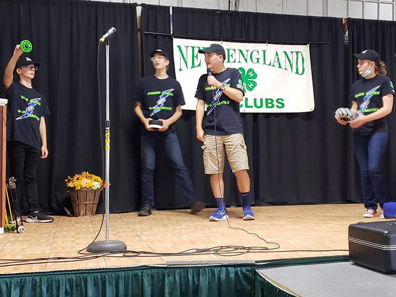 Four students on stage demonstrating different kinds of robot wheels