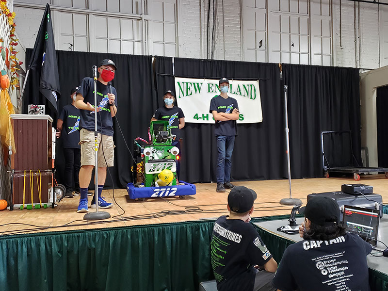 three students on stage at BigE demonstrating robot