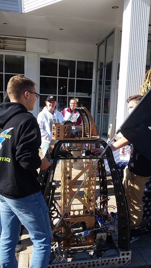 Students in parking lot of grocery store with robot at food drive event