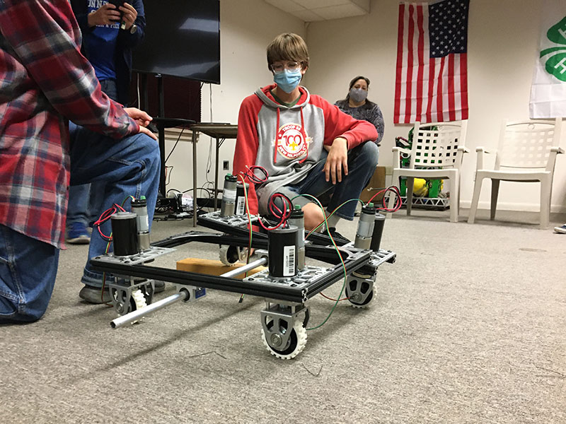 Two students kneeling next to robot chassis demonstrating drivetrain.