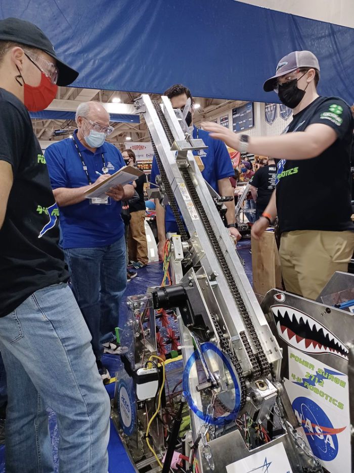 students showing the robot climbing mechanism to judges at a competition