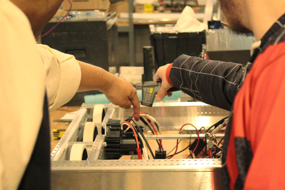 close up of hands of student and mentor taking temperature of electronic component on robot