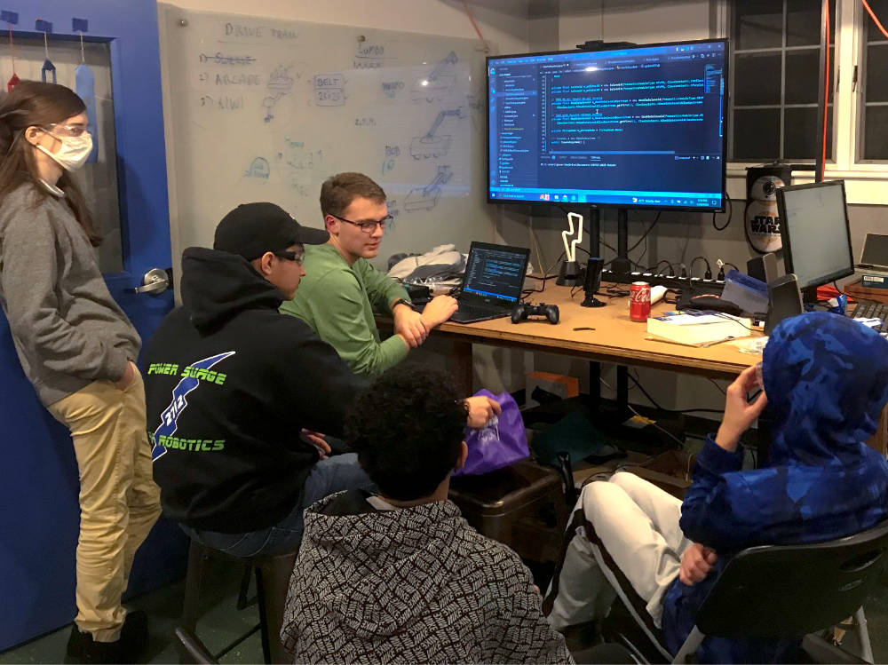 four students in front of large monitor discussing programming code